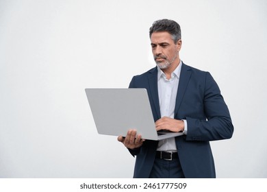Serious handsome latin older man in formal suit holding desktop computer. Portrait of focused middle age mature businessman using pc laptop for business work. Isolated white background, copy space