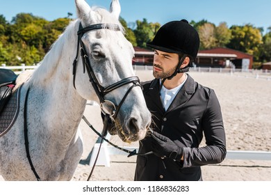 Serious Handsome Male Equestrian Fixing Horse Halter At Horse Club