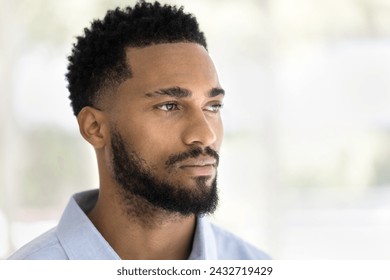 Serious handsome young African man indoor casual portrait. Thoughtful dreamy barber model, Black guy with stylish beard posing indoors, looking away in deep thoughts. Close up shot - Powered by Shutterstock