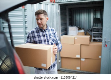 Serious Handsome Young Man In Casual Clothing Finding Place In Car For Cardboard Box While Loading Automobile At Container Storage Area, He Storing Things In Container