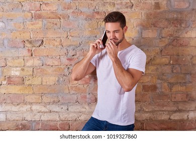 A serious handsome young man talking on his phone in a white tshirt.