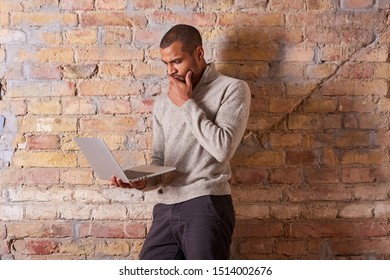 A serious handsome young man using a laptop in a sweater.