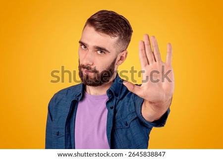 Serious hipster guy gesturing STOP, showing palm to camera over grey studio background
