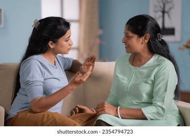 Serious indian adult daughter with mother discussing by talking each other while sitting on sofa at home - concept of parent guidance, communication and family bonding - Powered by Shutterstock