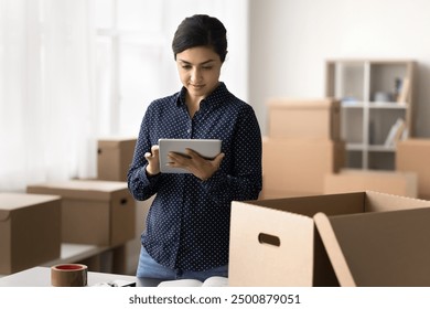 Serious Indian warehouse worker hold digital tablet, manage stock inventory, contact to courier, organize delivery service dispatch of goods to clients, small business owner workflow using modern tech - Powered by Shutterstock