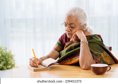 Serious Indian Woman Writing Or Sketching Something In The Notebook