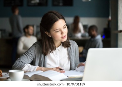 Serious intelligent millennial girl studying in cafe or student canteen preparing for exam test or coursework, doing home assignment, reading notes in exercise book, knowledge and education concept