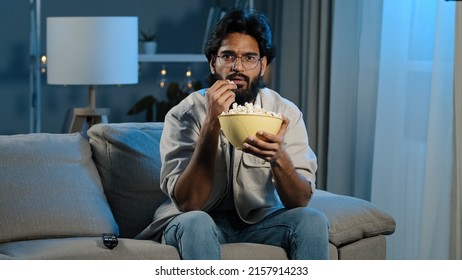 Serious interested Arabic Hispanic Indian bearded man guy wearing glasses 30s male with popcorn watching TV at home sofa late evening night relaxing enjoying movie online sport game attentively watch - Shutterstock ID 2157914233