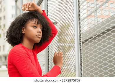 Serious and introspective young woman leaning on a wire fence, lost in thought and contemplation - Powered by Shutterstock