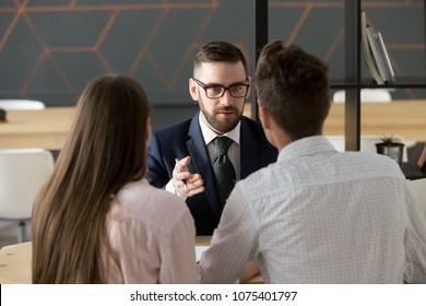 Serious investment broker, financial advisor or bank worker in suit and glasses consulting young couple giving legal advice, offering loan or presenting insurance services convincing to make deal
