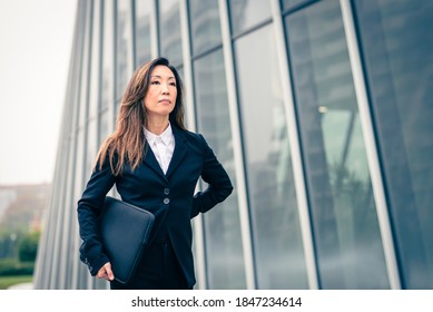 Serious Japanese Businesswoman Walking Beside A Skyscraper, Woman CEO Of High Finance Walking In The City, Concept Of Female Affirmation In The World Of Finance, Success Without Gender Discrimination