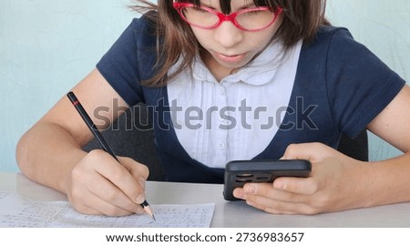 Serious kid doing classwork using smartphone in class and mobile education. Exam cheat sheet