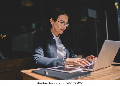 Serious Lady In Formal Wear And Glasses Typing On Laptop Keyboard While Sitting At Restaurant Table And Working On Business Project