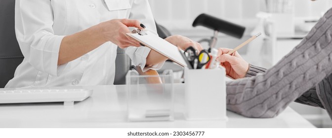 Serious lady signing informed consent form in presence of smiling friendly healthcare worker - Shutterstock ID 2303456777