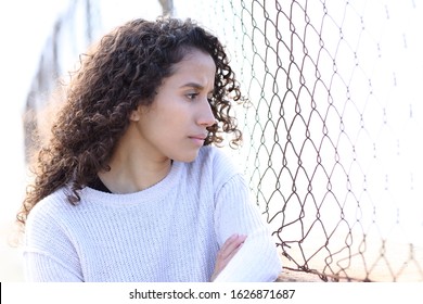 Serious latina girl looking away through a grid standing in the street