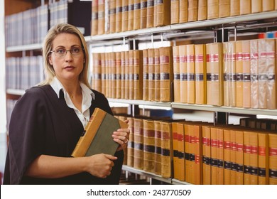 Serious lawyer holding a book in library - Powered by Shutterstock