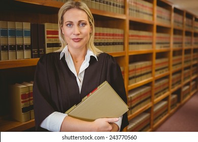 Serious lawyer holding a file while standing in library - Powered by Shutterstock