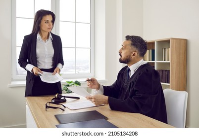 Serious Lawyer Talking To The Judge In The Courthouse. Young Female Attorney And Male Judge Discussing Legal Interpretation During A Trial Process In A Court Of Law