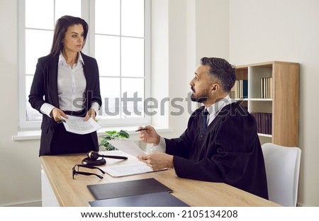 Serious lawyer talking to the judge in the courthouse. Young female attorney and male judge discussing legal interpretation during a trial process in a court of law