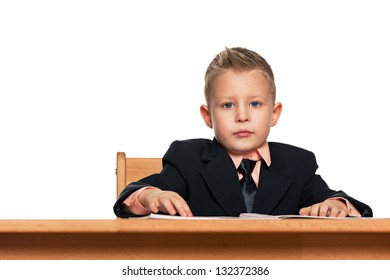 Serious Little Boy In Suit Sits At The Desk Alone