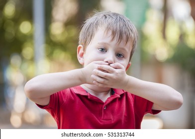 Serious little Caucasian boy closing his mouth with hands. Illustrative image for childhood trauma, child traumatic experience. Psychological assistance, children rescue. Silent cry for help. Stutter