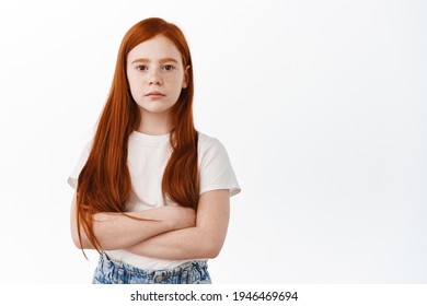 Serious Little Girl With Ginger Hair Cross Arms On Chest And Look Determined. Cofident Redhead Kid With Freckles Staring Focused At Camera, White Background