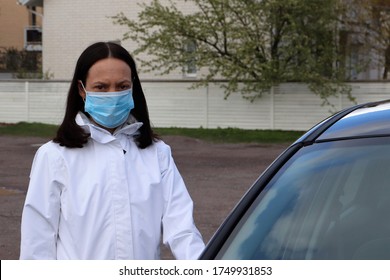 A Serious Looking Brunette Female With A Disposable Face Mask Standing Next To A Car. She Is On The Way To Run Her Errands And She Is Worried About The Corona Virus.