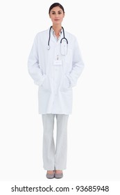 Serious Looking Female Doctor With Hands In Her Pockets Against A White Background