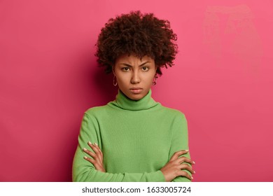 Serious Looking Offended Woman Looks Angrily At Camera, Keeps Arms Folded, Smirks Face, Doesnt Trust Person, Dressed Casually, Isolated On Pink Wall, Dislikes Suspicious Idea, Disagrees With Someone