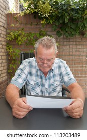 Serious Looking Senior Man Reading A Document In His Backyard