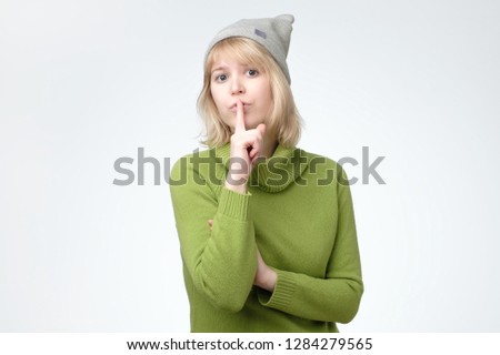 Serious lovely female asks to keep secret information confidential, dressed in green sweater and hat. Conspiracy concept