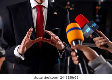 Serious male American politician talks with journalists, answers questions and gives interview for media and television news in government building. United States congressman during press conference.