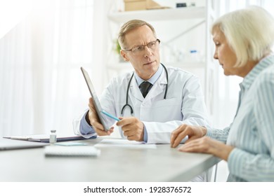 Serious Male Doctor Having Appointment With Old Woman In Clinic