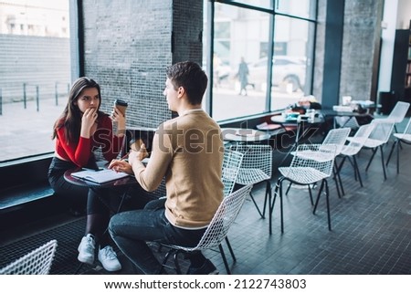 Serious male and female college students in casual clothes having coffee break in empty cafeteria after working on project together