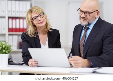 Serious Male And Female Executives With Calm Expression Working Together On Laptop Computer Behind White Table With Little Plant Nearby In Office