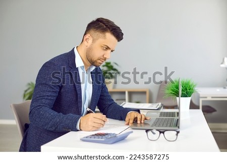 Serious male financial director of business company is engaged in budget analysis and calculations. Side view of man at his workplace working with laptop, paper documents and calculator.