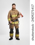 Serious male firefighter in uniform holding big axe for work. Front view of dark-haired man in fireman apparel posing with wooden hatchet tool, on gray studio background. Job, equipment, tool concept.