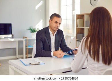 Serious Male HR Manager Interviewing Female Job Candidate Asking Her Questions Concerning The Experience She Stated On Her Resume. Strict Employer Talking To Employee Sitting At Desk In The Office