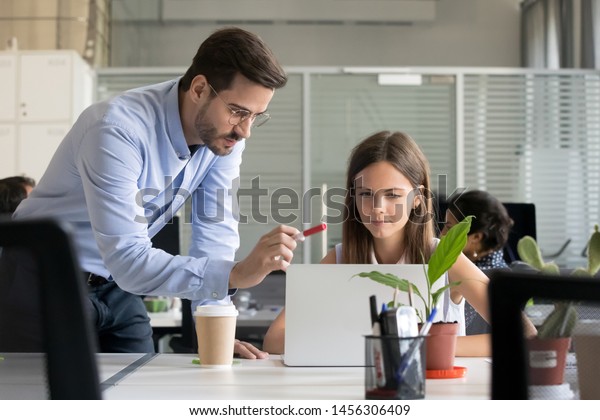 Serious male manager in glasses teach young\
female intern working at laptop, explain issues pointing, man\
trainer or coach instruct girl trainee helping with project, give\
instructions or\
correcting
