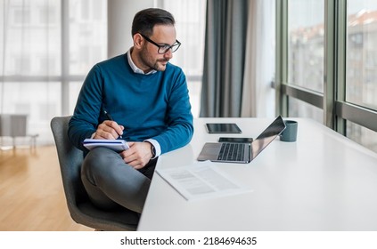 Serious male manager making notes in diary. Young entrepreneur is planning strategy while working at desk. He is wearing smart casuals in office. - Shutterstock ID 2184694635