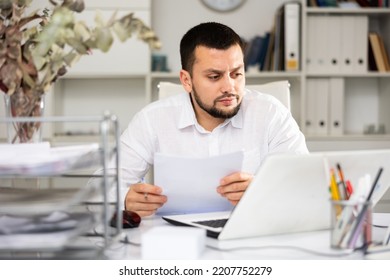 Serious Male Office Worker Sitting At Desk And Doing Paperwork.