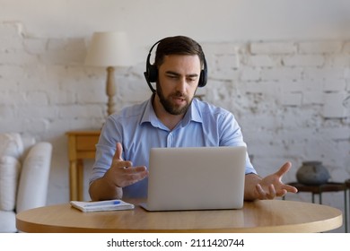Serious male online teacher in headphones speaking at mic, using laptop, presenting tutorials to student audience on online conference, video call. Employee working from home, talking to client