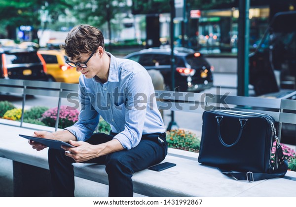 Serious male owner reading received notification
with receipt on touch pad during time in financial district,
businessman in formal wear using banking app digital tablet for
checking balance
account