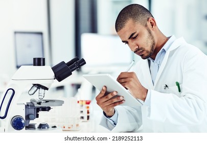 Serious Male Scientist Working On A Tablet Reviewing An Online Phd Publication In A Lab. Laboratory Worker Updating Health Data For A Science Journal. Medical Professional Document Clinical Trial