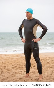 Serious Male Swimmer Standing On Beach. Full Length View Of Middle Aged Sportsman In Wetsuit Standing On Sea Coast After Competition. Triathlon Concept