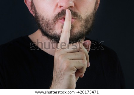Serious man with beard and mustache making silence gesture, pst, shh, face detail