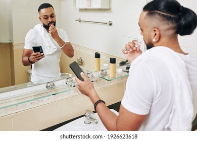 Serious man brushing teeth in bathroom and reading news on smartphone screen - Powered by Shutterstock