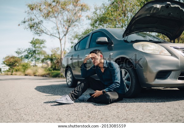 Serious man headache sitting beside car\
breakdown on roadside. Car broken\
concept.