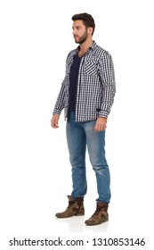 Serious man in jeans, boots and unbuttoned lumberjack shirt is standing and looking away. Full length studio shot isolated on white.