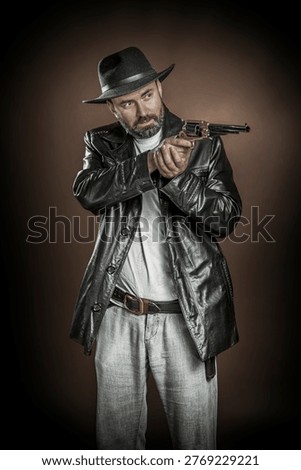 Serious man in a leather jacket posing as a wild west outlaw, studio portrait